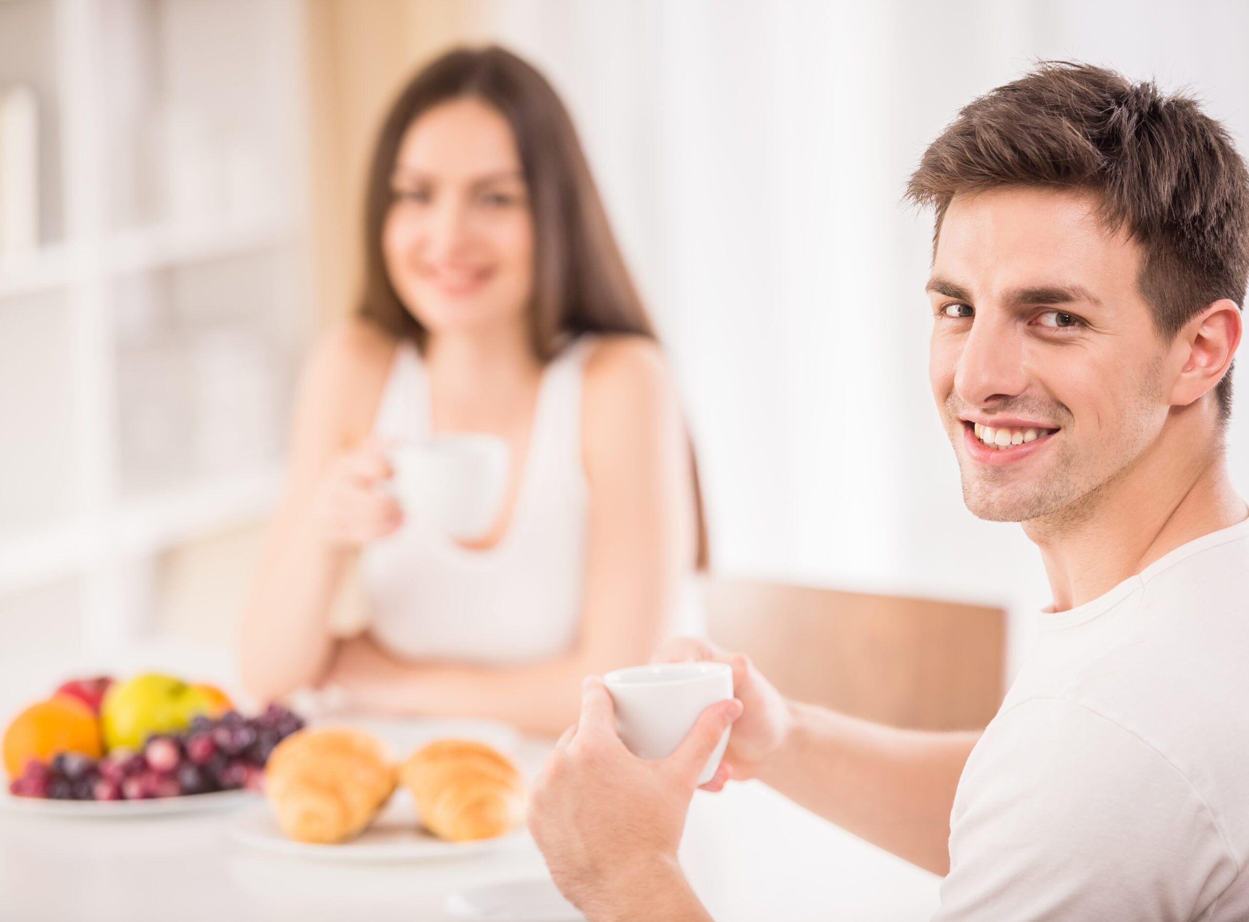 Young family couple sitting at the table in the kitchen and having breakfast together.